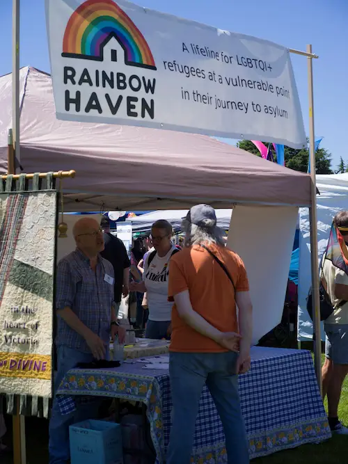 Brian speaking to a visitor at one side of the booth while another visitor inspects the literature on display. The banner on the left belongs to our sponsor the Anglican Church of S. John the Divine Victoria. 
